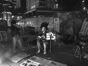 Father Franco Mella performing on guitar at the ‘Occupy’ protest camp in the public plaza beneath the Hong Kong and Shanghai Bank headquarters, Central, 12 December 2011