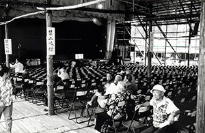 People sitting in a matshed theatre: scene during a once-every-ten-years purification ceremony at Shek O, 26 October 1996