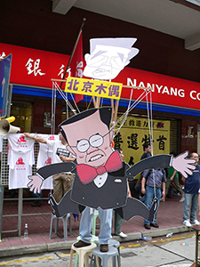 Hong Kong's Chief Executive Donald Tsang being portrayed as a puppet of Beijing (in the form of Chinese leader Hu Jintao), alongside the democracy march between Causeway Bay and Wanchai, 1 July 2005