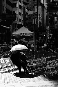 People sheltering from strong sun under an umbrella, Sheung Wan Cultural Square, 14 December 2014