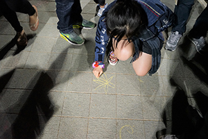 A woman writes graffiti on the ground, Tamar Park, Admiralty, 1 January 2015