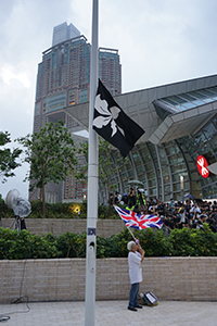 Black Bauhinia flag on a flagpole, with 'Grandma Wong' waving a British flag, West Kowloon Station, 7 July 2019
